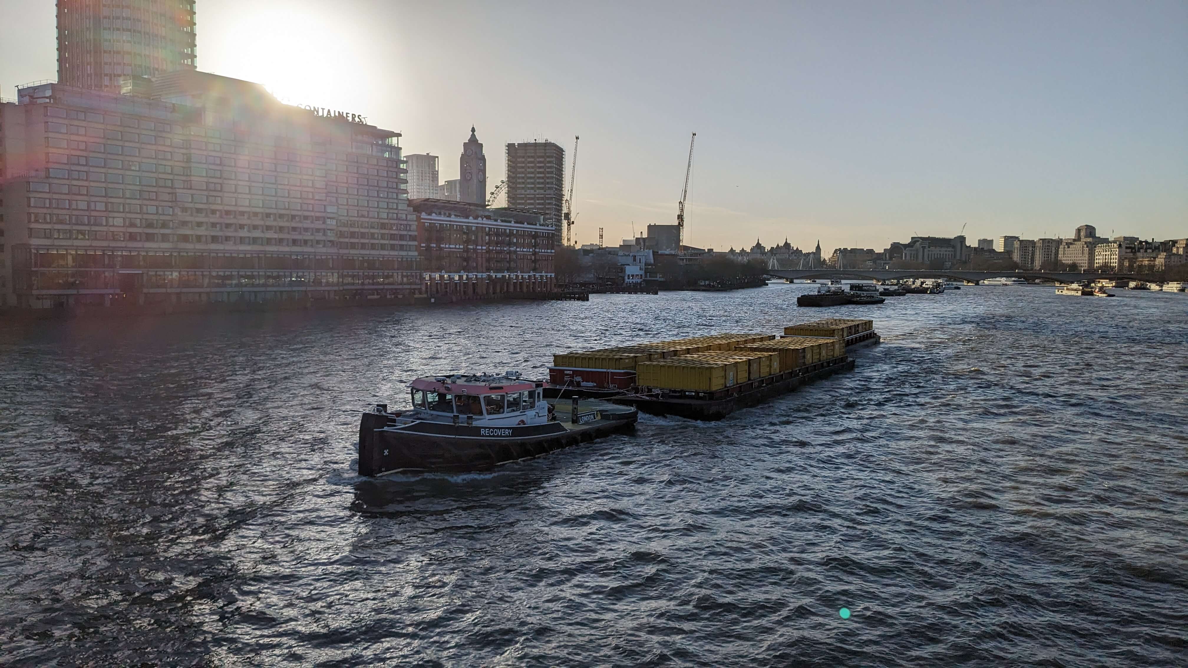 A boat on the river Thames, taken from Blackfriars Bridge facing westward. In the background are the south bank buildings and the sky is blue.
